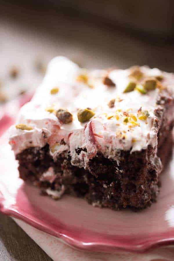 Chocolate poke cake filled with a cherry syrup and chocolate then topped with a creamy cherry topping! Pistachio nuts are sprinkled over top. lemonsforlulu.com