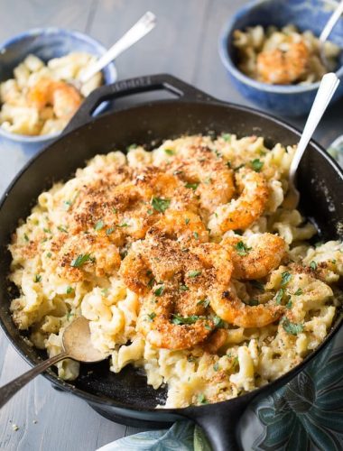 Cast iron skillet with Cajun Shrimp Mac and Cheese with a silver spoon on a wooden table.
