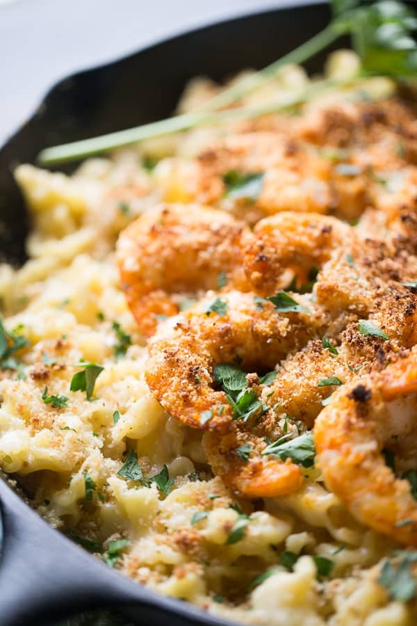 Close up of juicy Cajun Shrimp on top of Mac and Cheese in a large cast iron skillet.