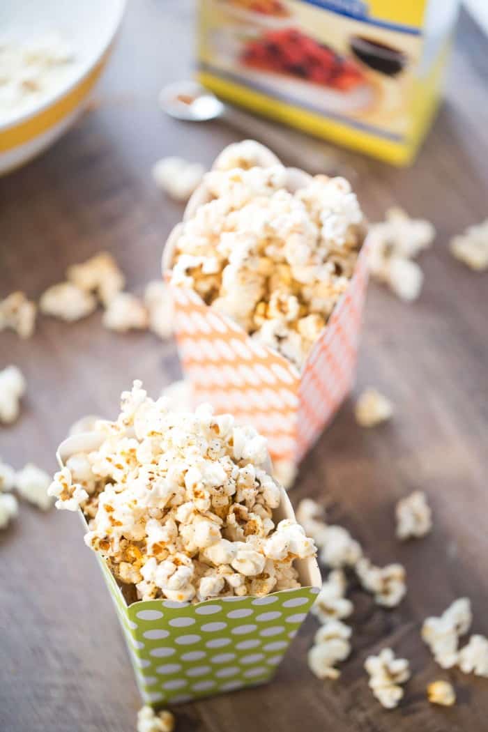 A smoky and sweet kettle corn in two green and orange popcorn containers on a wooden table. 