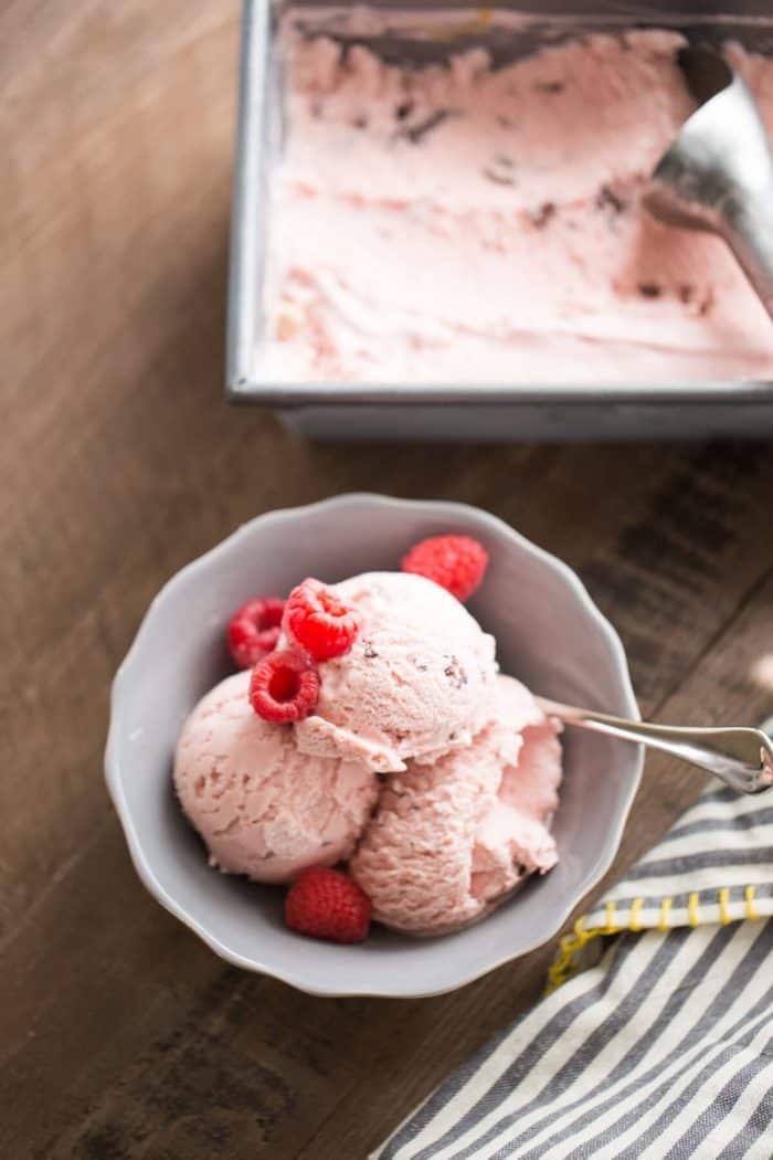 Creamy raspberry ice cream topped with fresh raspberries in a small bowl with a silver spoon.