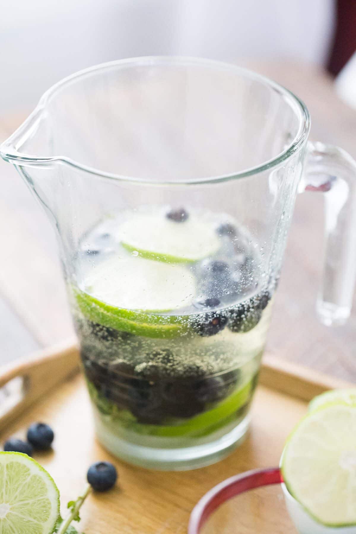 Homemade Blueberry Mojito in a pitcher with blueberries and sliced limes.