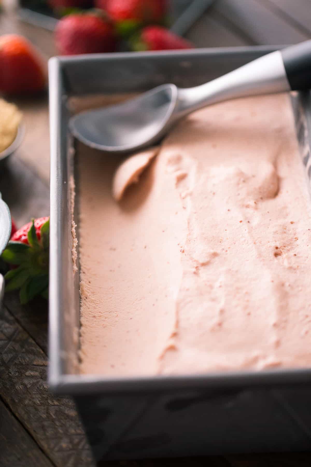 Scooped Basic Brown Sugar Strawberry Ice Cream recipe next to fresh strawberries on a wooden table.