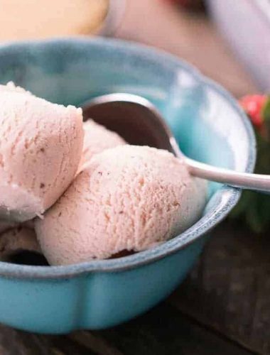 Three scoops of Delicious Brown Sugar Strawberry Ice Cream in a blue bowl on a wooden table.