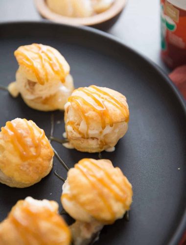 Five profiterole treats drizzled with caramel on a black serving plate.