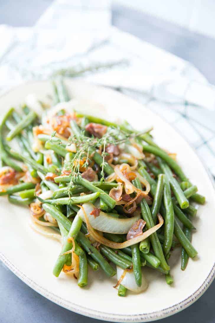 Delicious Green Beans recipe with balsamic dressing and caramelized onions on a white serving platter.