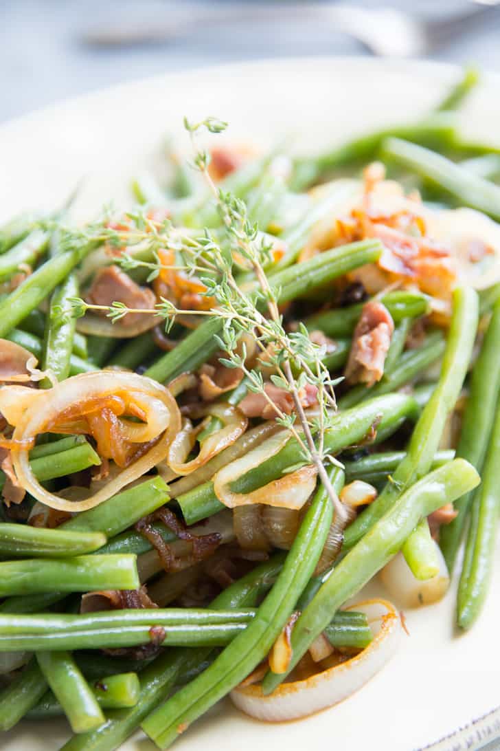 Closeup of Balsamic Green Beans with caramelized onions,, garnished with rosemary on a white serving platter.