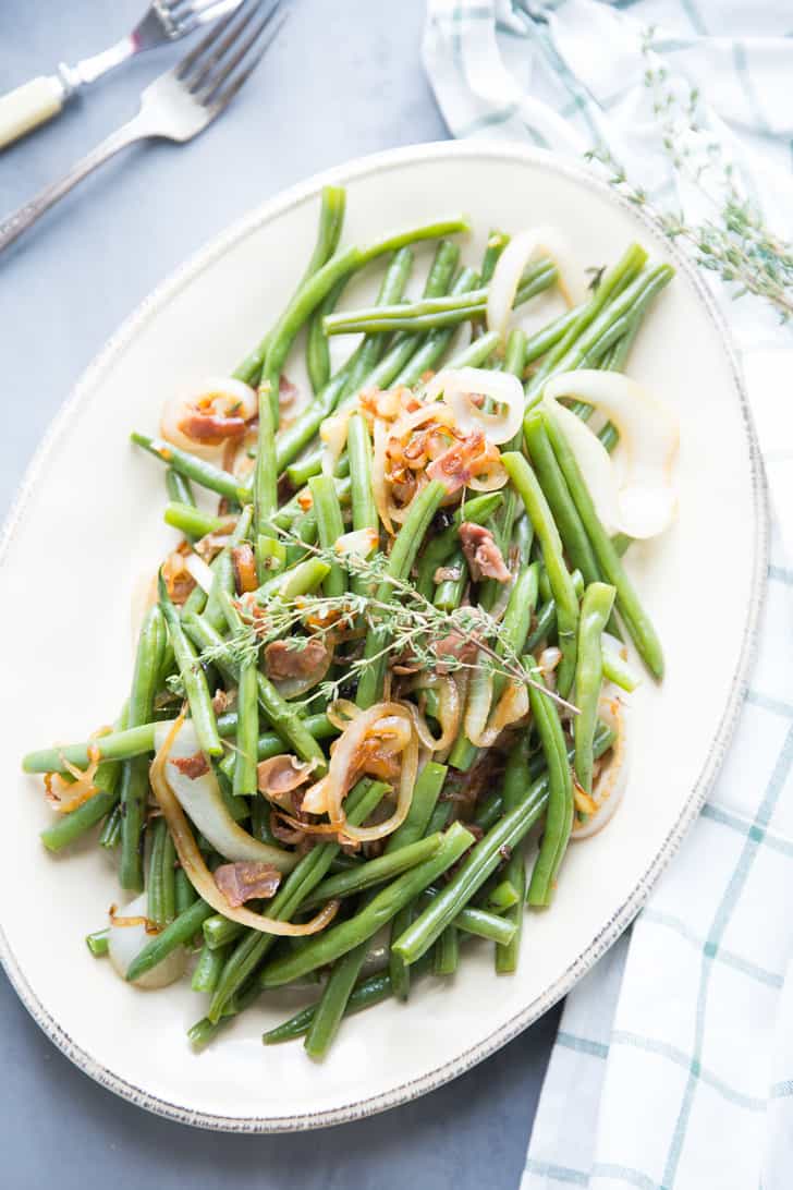 Delicious Balsamic Green Beans dish with caramelized onions on a white serving platter on a blue table.
