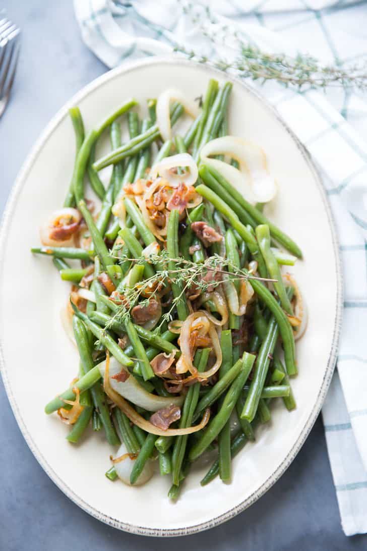 Delicious Green Beans with balsamic dressing with caramelized onions, garnished with rosemary on a white serving platter.