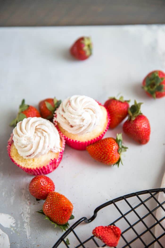 Two strawberry cupcakes surrounded by strawberries