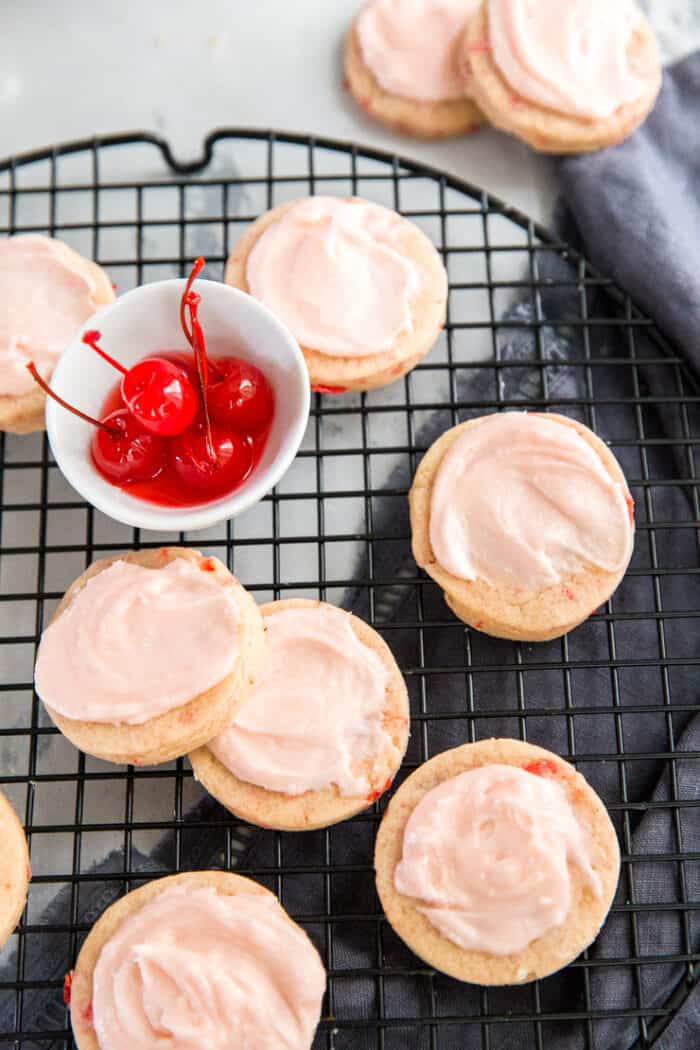 sugar cookies arranged on a baking sheet with a bowl of cherries