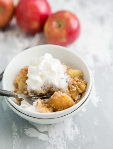 apple crisp in a bowl with whipped cream and a fork