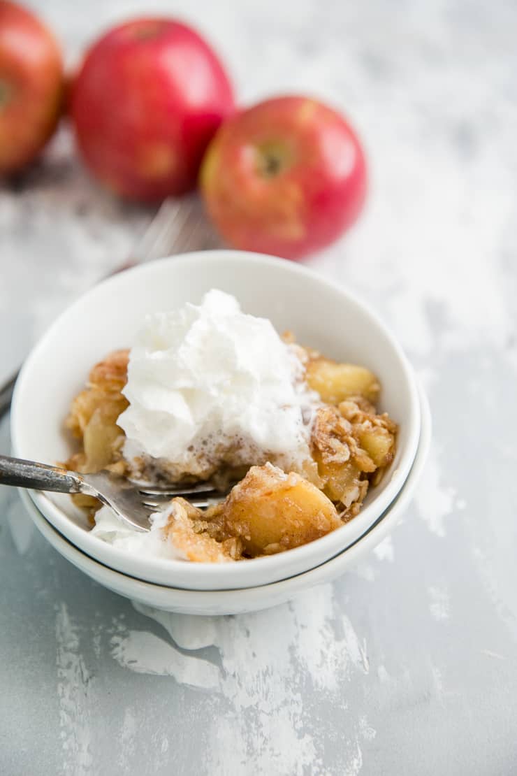 apple crisp in a bowl with whipped cream and a fork