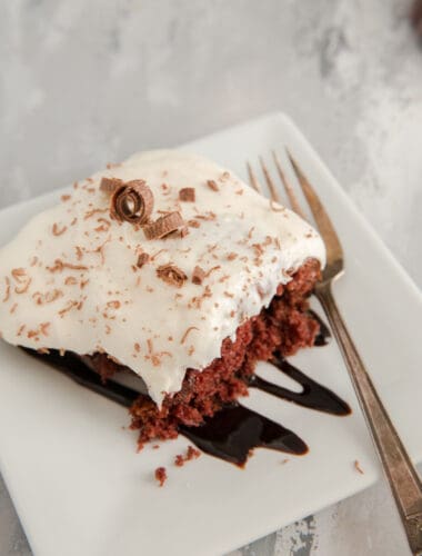 poke cake on a white plate with chocolate sauce
