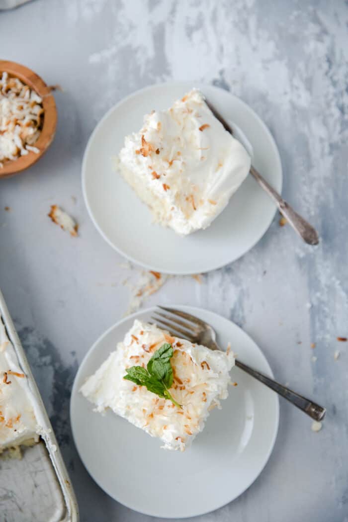 two slices of coconut cream cake on white plates