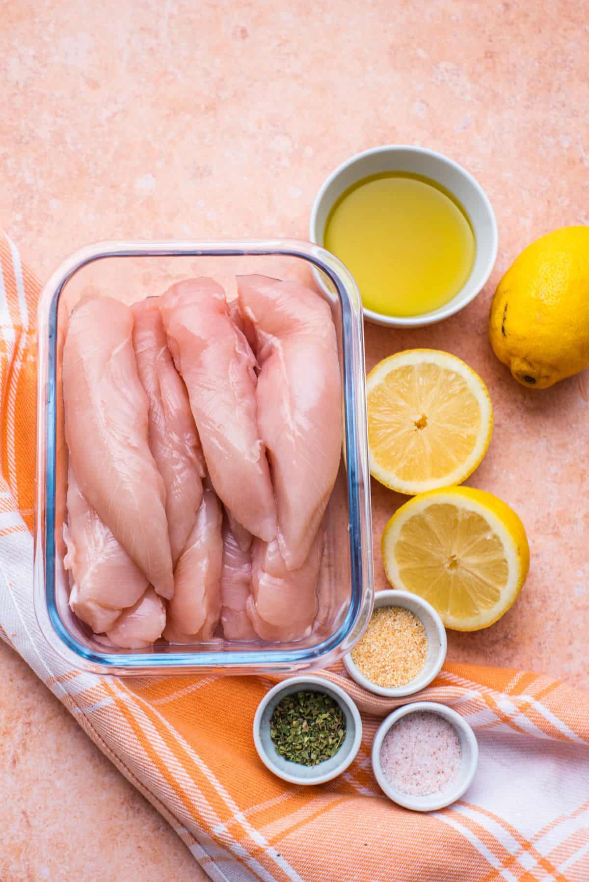 raw chicken strips in a glass container olive oil sliced lemon and seasonings
