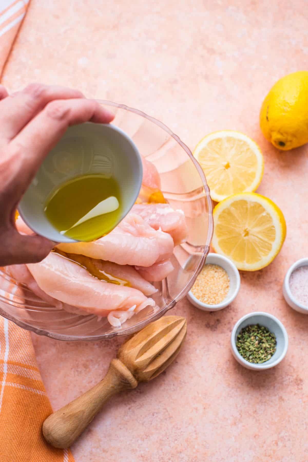 pour olive oil over raw chicken in bowl