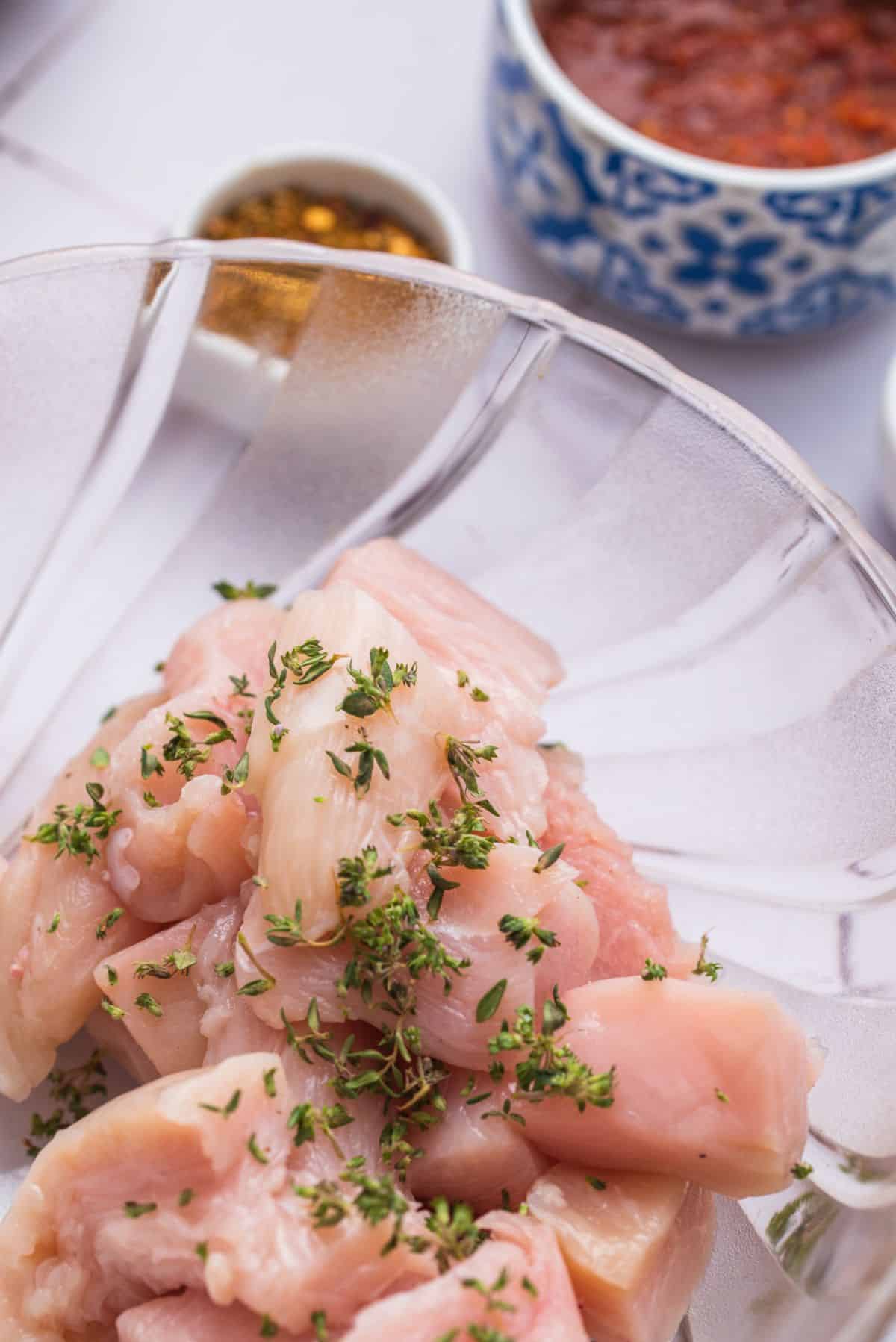 pieces of raw chicken in bowl with thyme