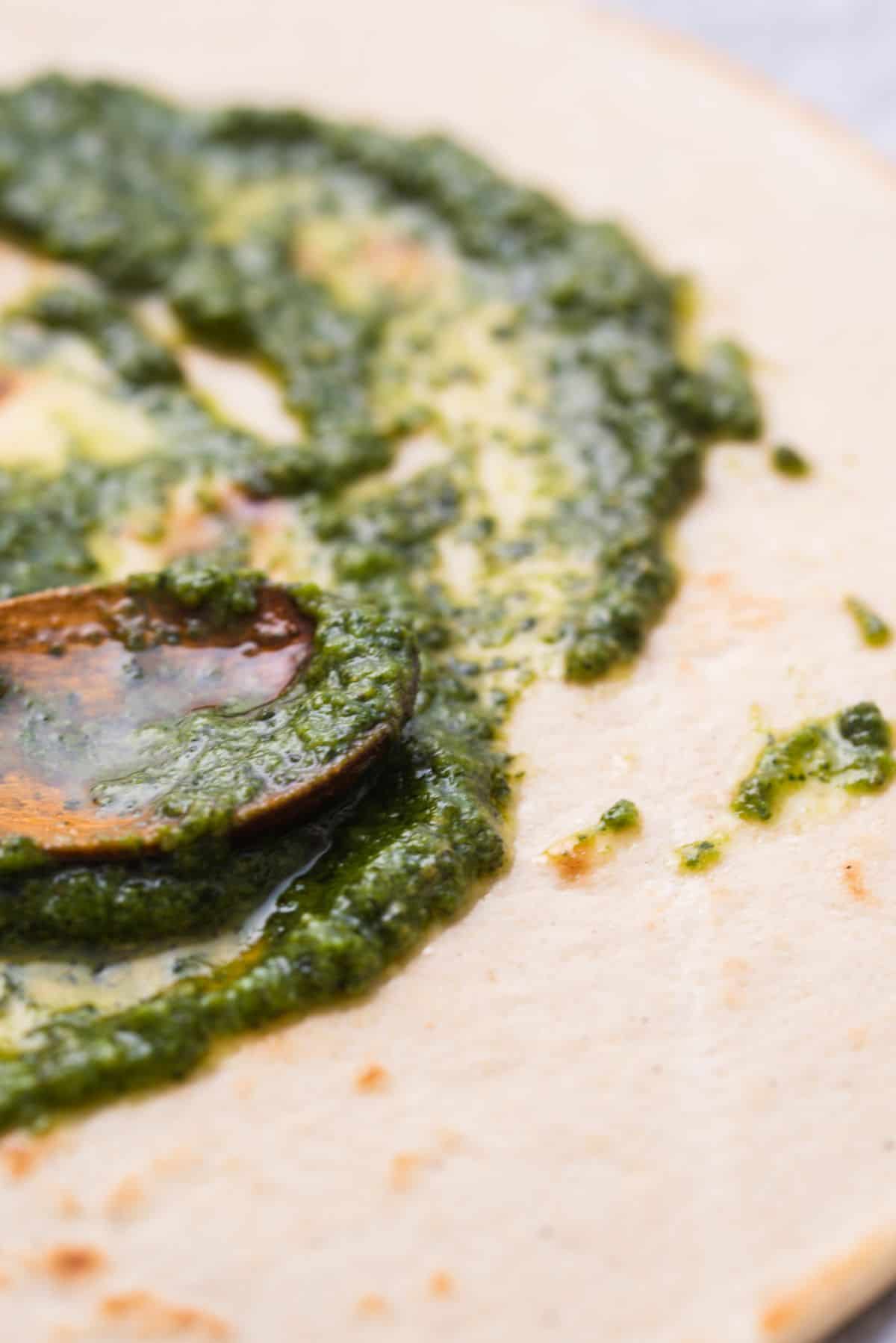 Pesto being spread with a spoon onto base of pizza