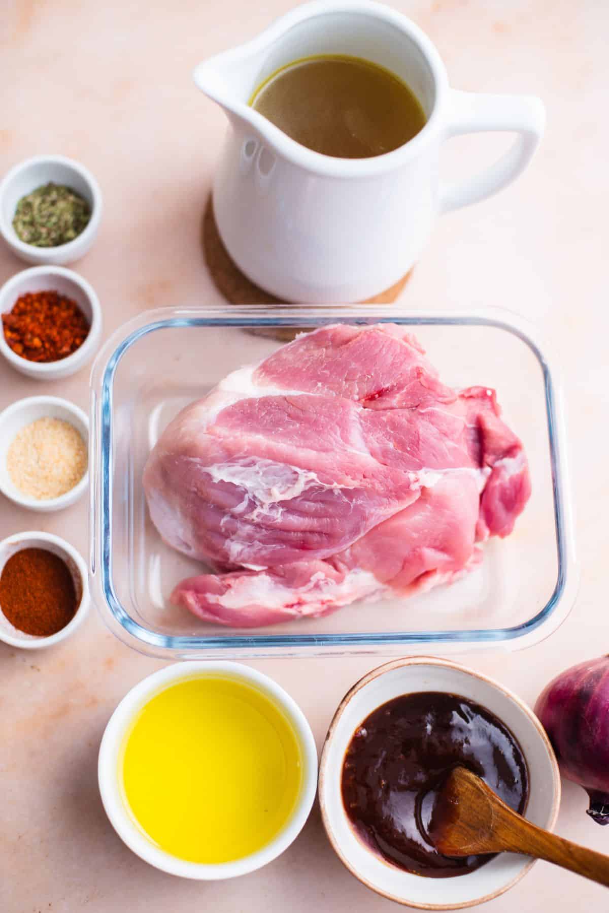 raw roast in glass container with small bowls of seasonings